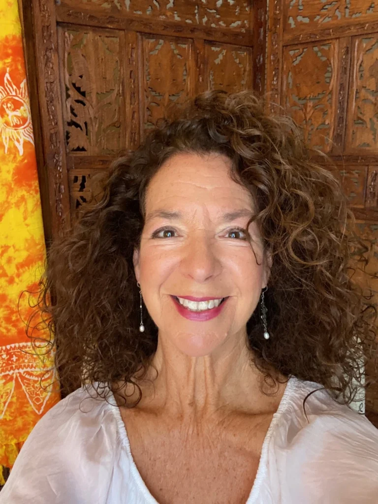 Valerie Varan smiling, in a white blouse in front of a carved wooden screen